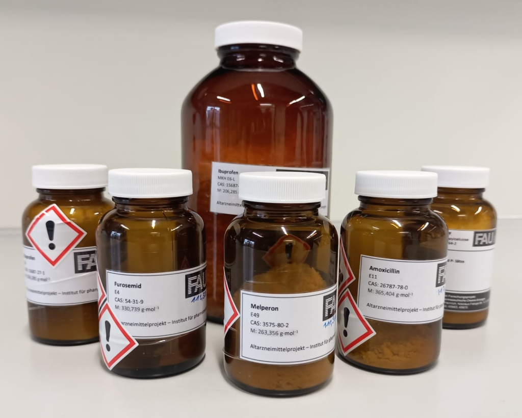 The photo shows 5 smaller brown glass bottles with white lids and white labels listing the chemical ingredients. In the middle of the five is a large brown glass bottle.